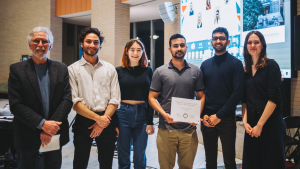 Six people standing and smiling while posing for a photo. One of them is holding a certificate. 