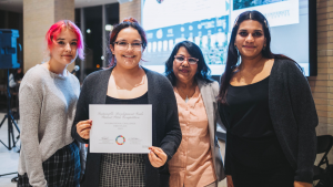  Four people posing for a photo. One of them is holding a certificate. 