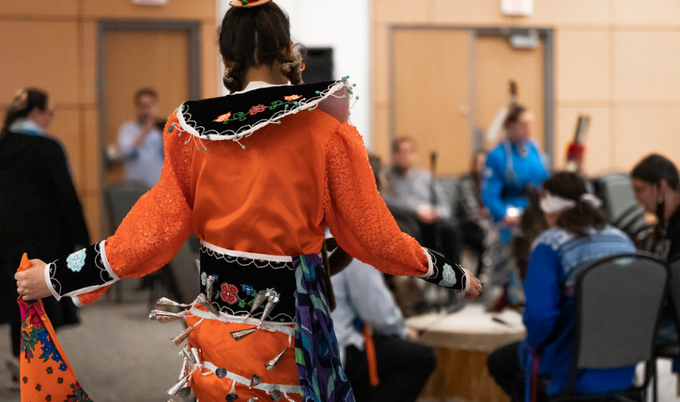 A dancer in traditional Indigenous clothing performing in front of a crowd of people 