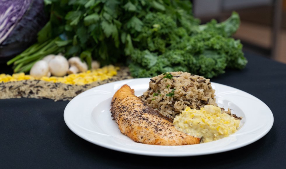 Sumac salmon plated with wild rice and corn in a white dish on a black tablecloth