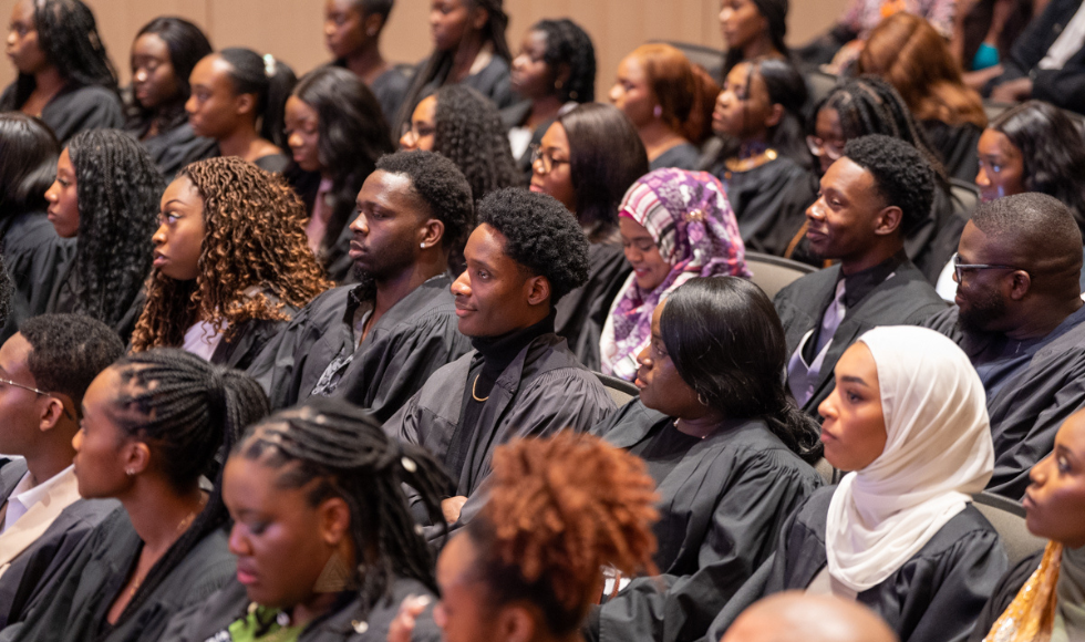 Students in graduation gowns watch the Black Excellence Graduation celebrations from their seats in LR Wilson Hall.