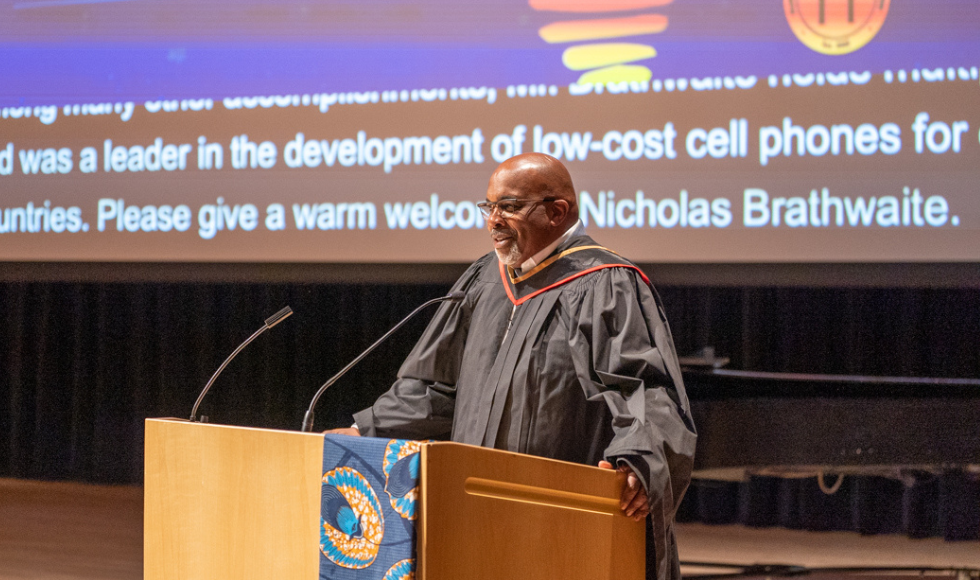 Nicholas Brathwaite speaks at the Black Excellence Graduation celebration podium, wearing academic regalia.