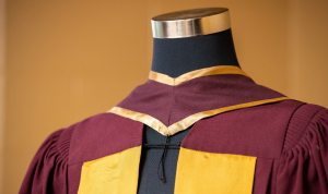 A maroon and gold convocation robe on a headless mannequin 