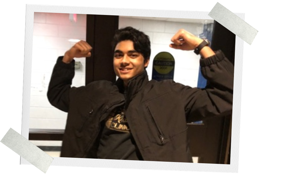 Taaha Hassan in his first year, wearing a jacket, has his arms up in a joking "strong man" pose.