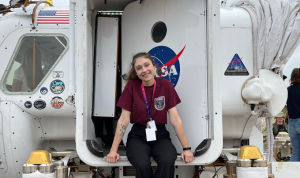 Taren Ginter sitting in the doorway of a spacecraft with a NASA logo.