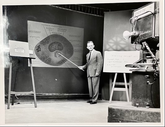 Black and white picture of a professor being videotaped teaching. 