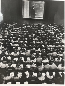 black and white image from the 1960s of a full lecture hall of students watching a class on a big screen.