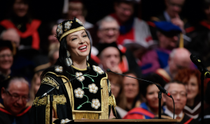 A smiling Santee Smith in her Chancellor's robe speaking at the podium on stage during convocation.