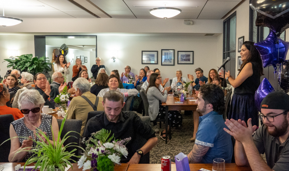 Shylo Elmayan speaks at the microphone to a packed room at the Buttery at the the 2023 Indigenous Graduation celebration.