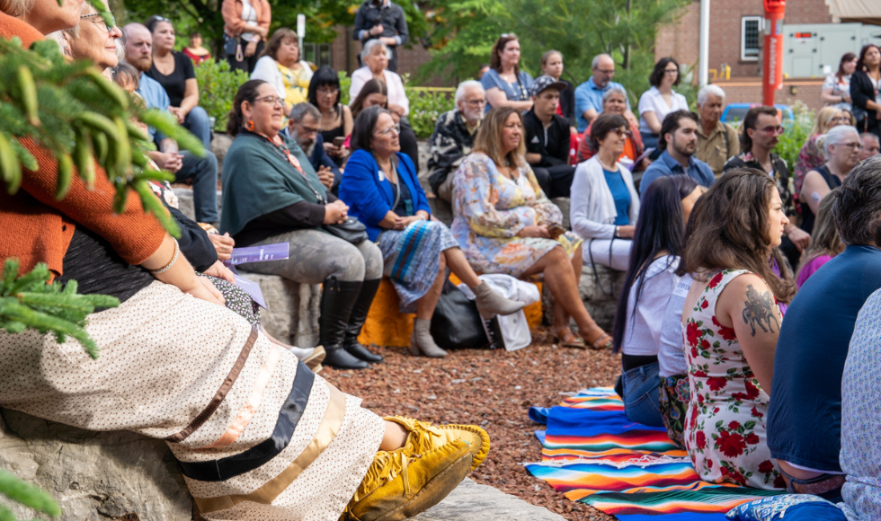 A large number of people sitting on the stones at the outdoor classroom.