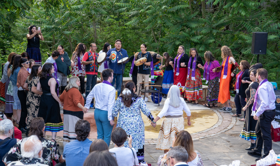 Students, loved ones, faculty and staff participate in a round dance in the outdoor classroom.