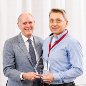 Krzysztof Adamczyk holding the President’s Award for Outstanding Service and posing for a photo with David Farrar