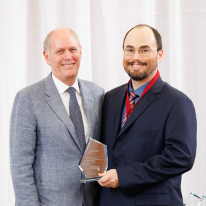 Omar Danta holding a President’s Award for Outstanding Service and posing for a photo with David Farrar