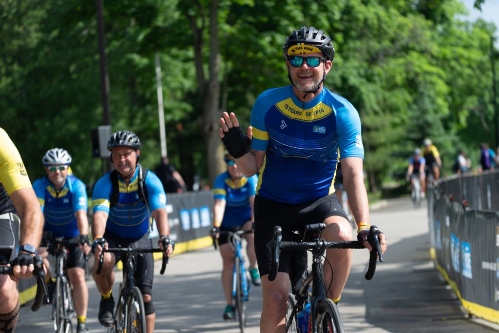 Bicyclists in Ride to Conquer Cancer gear smiling during a sunny ride.