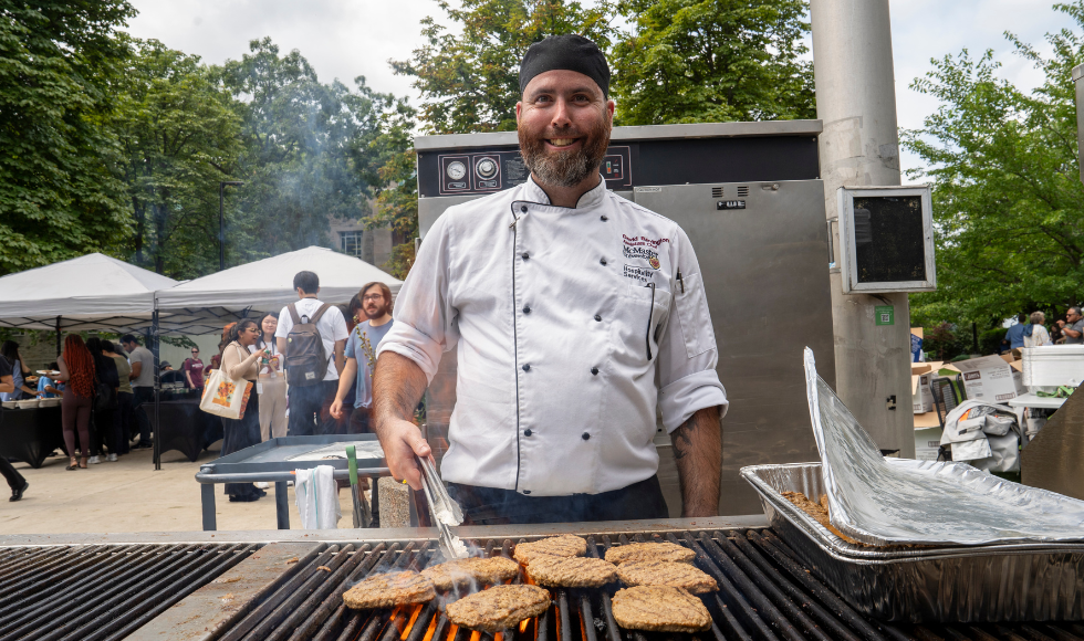 A person in a Hospitality Services work jacket serving burgers at the employee picnic.