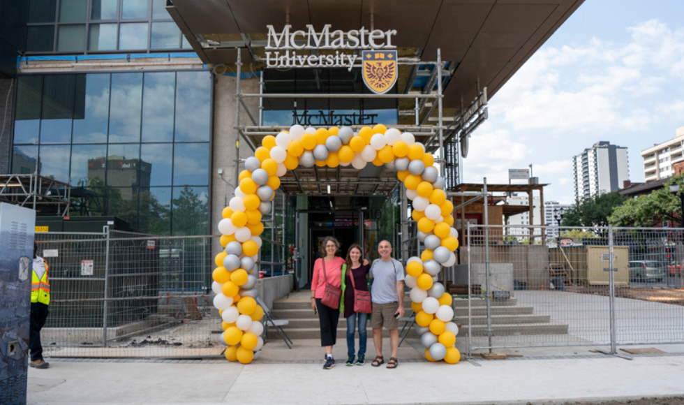 Three people posing under a balloon arch. Behind them, there is a sign that reads McMaster University 