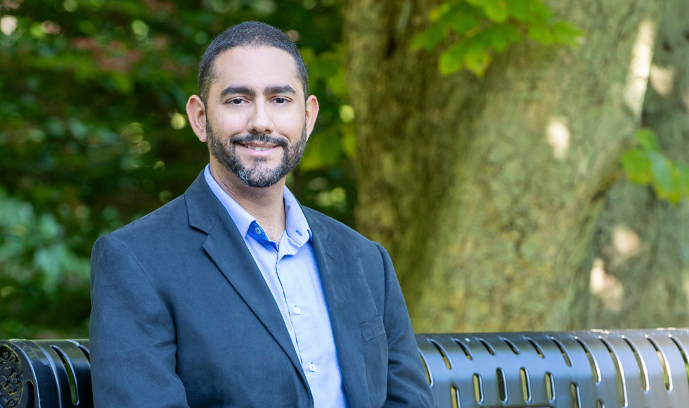 A man in a suit jacket seated on a bench smiling at the camera