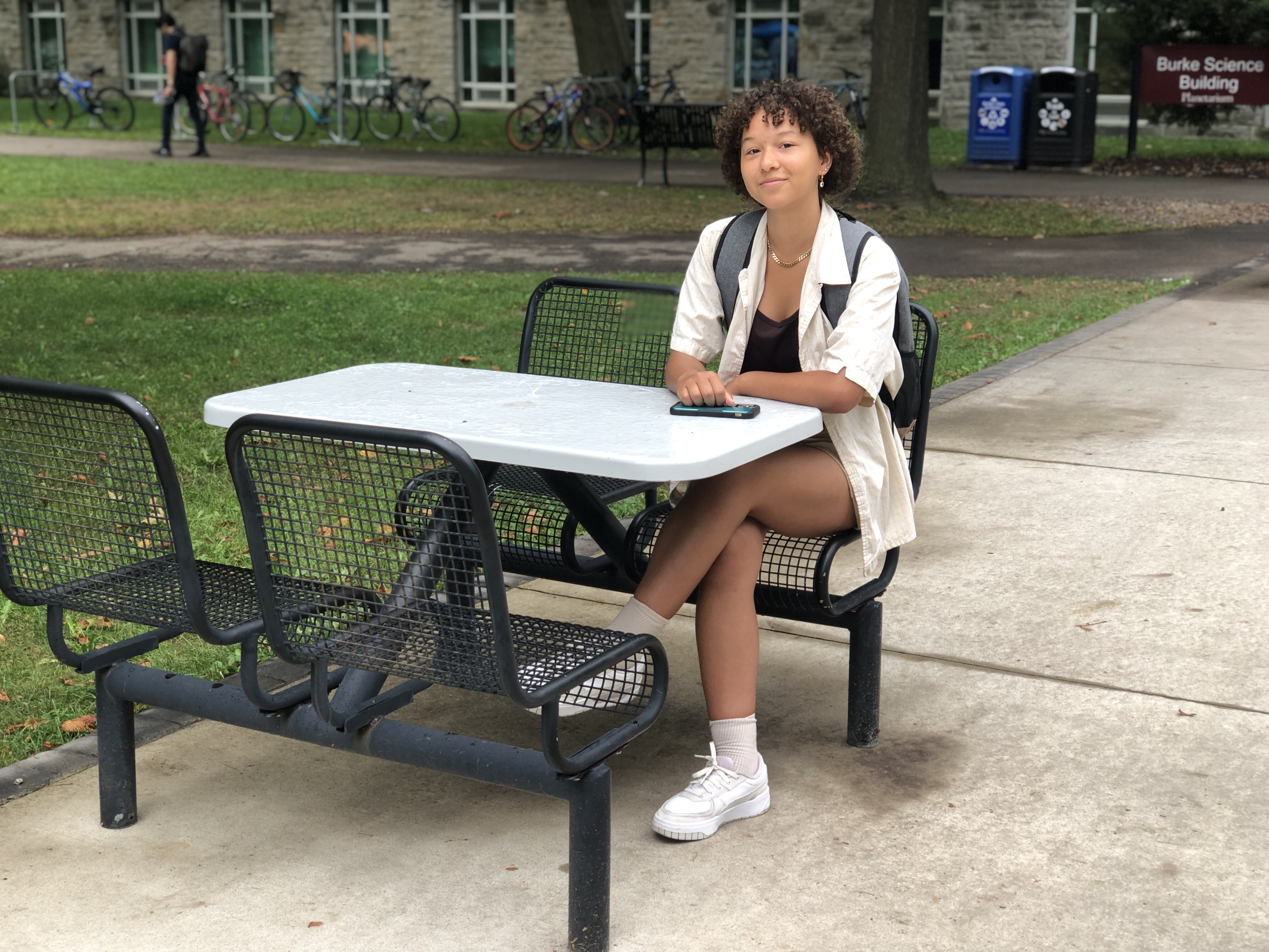 A person wearing a backpack seated at an outdoor table 