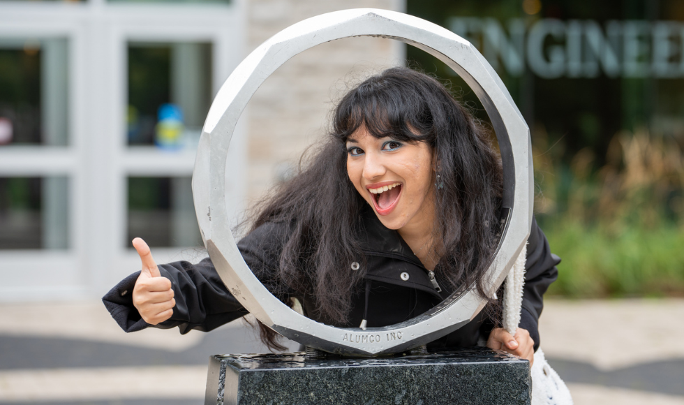 Danielle looking through the iron ring outside the Faculty of Engineering, smiling and giving a thumbs up.