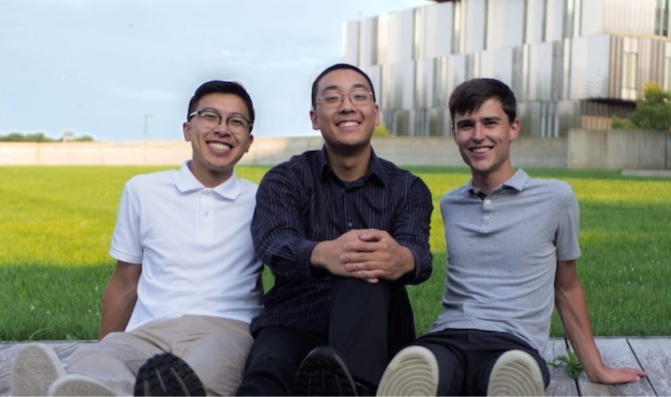 Three young people sitting on the ground smiling.