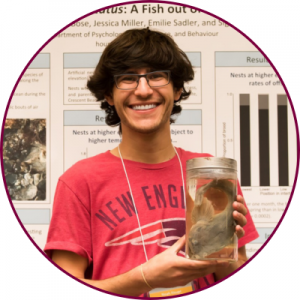 Noah Houpt holding a glass jar holding a fish while standing in front of an academic poster presentation