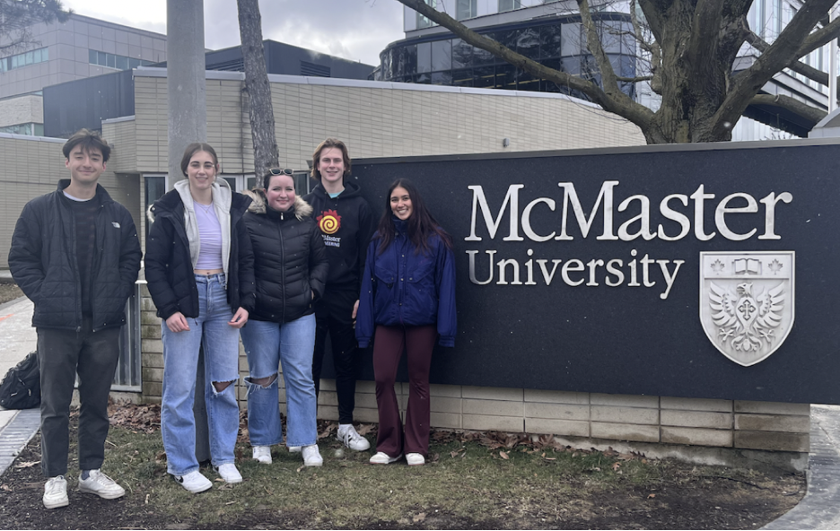 Five students standing in front of a McMaster University sign