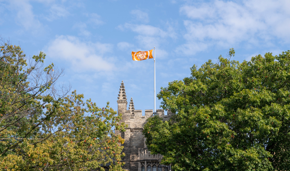 Orange Survivor's flag flies against a blue sky above University Hall.