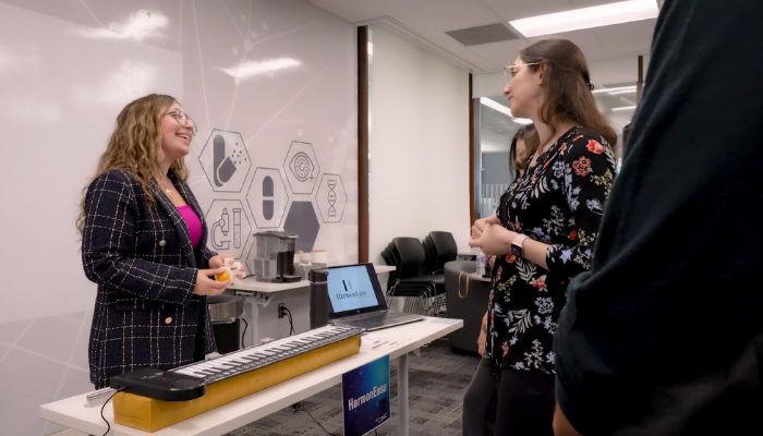 A smiling Deena standing behind a keyboard, chatting with a person about her invention.