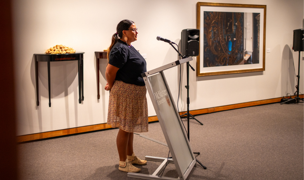 Katelyn Knott speaking into a microphone in a room inside the art gallery on campus.