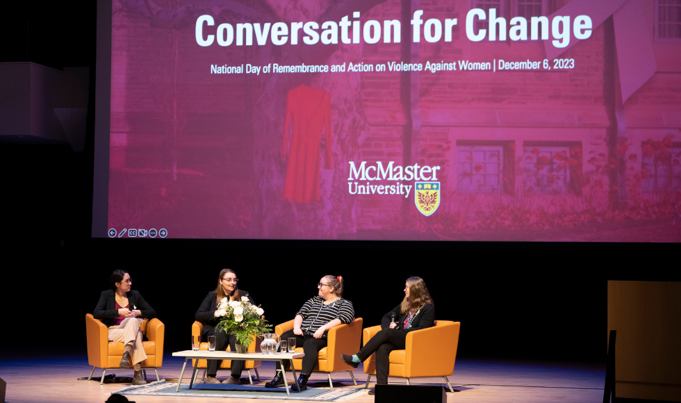 Four women sitting on stage in front of a massive screen that reads: Conversation for Change