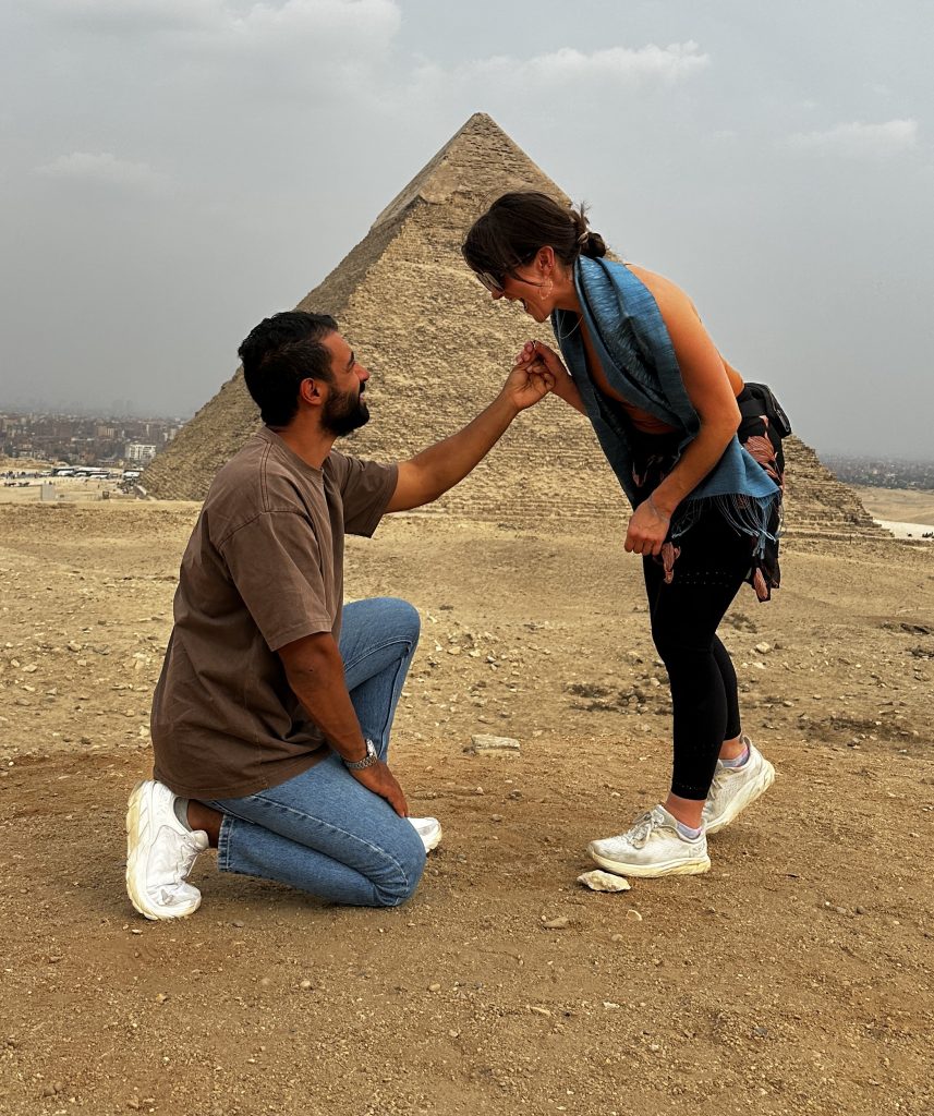 Safi down on one knee, asking Sydney to marry him. The Great Pyramid is in the background.