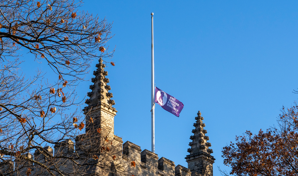 A purple flag with white letters that read "End Gender-based violence" hangs at half-mast at the top of University Hall