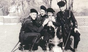 A black and white photo of Ross Mason and three other troops wearing military uniforms. They are holding a trophy.