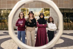 Four female students standing in front of the Eng building, seen through the iron ring.