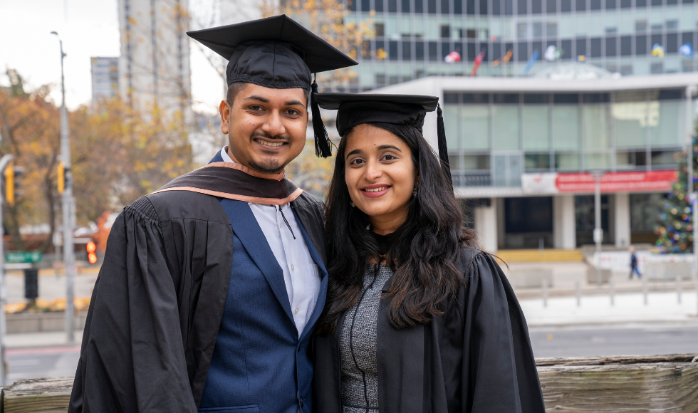 Two people smiling and wearing convocation gowns and mortarboards