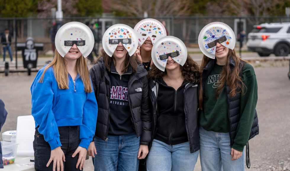 5 women wearing eclipse glasses holder made of paper plates they decorated.