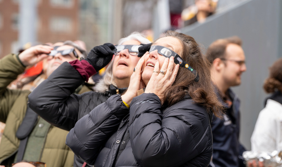Two women look upward while wearing eclipse glasses.