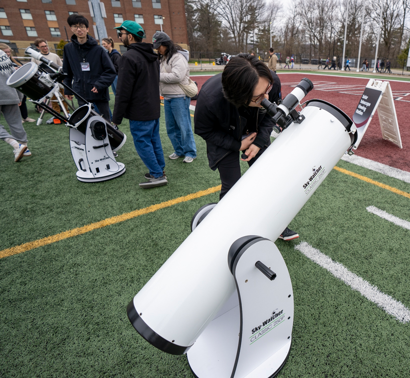 Graduate student Jinoo Kim looks into the eyepiece of a telescope on the field.