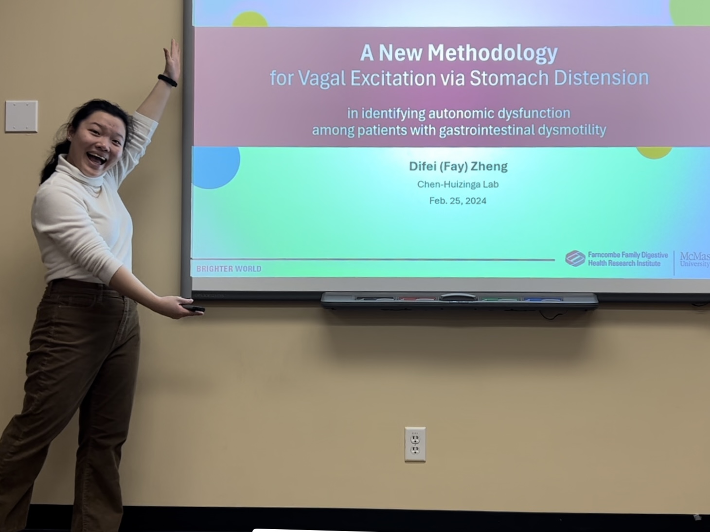 Difei (Fay) Zheng posing by a screen that is displaying a PowerPoint presentation 