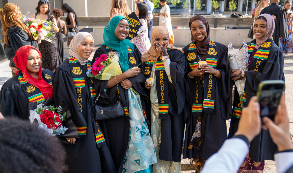 A group of students in gowns and Kente stoles smile for a group photo