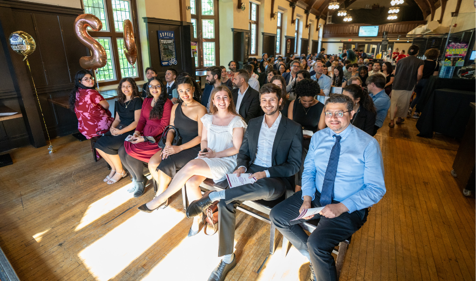 Rows of people seated. The first row of people are smiling at looking at the camera.