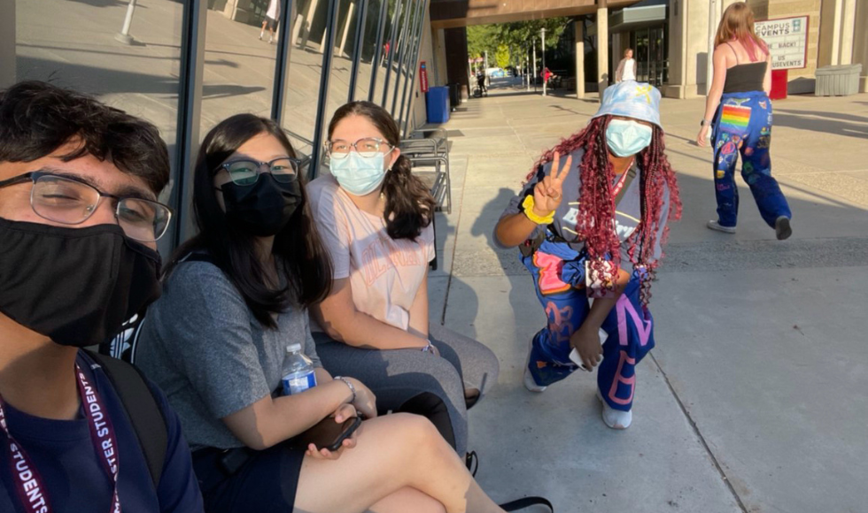 Four masked students, including one wearing colourful Welcome Week gear, posing for a photo