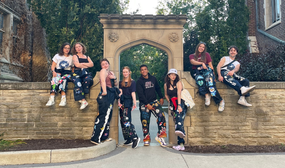 Eight students in navy Welcome Week gear pose for a photo by the Edwards Arch on McMaster’s campus 