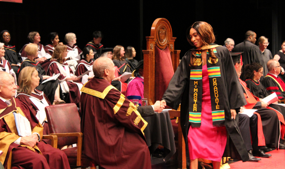 A student wearing a Kente stole and convocation gown shakes the hand of McMaster's president David Farrar 