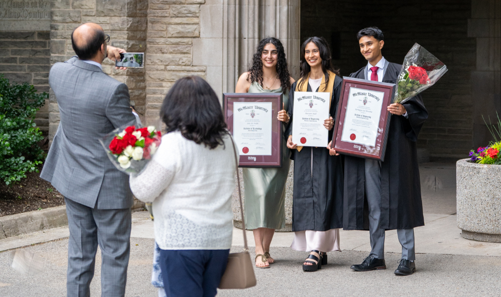 Three people holding framed degrees smiling as another person takes their photo on a cellphone 