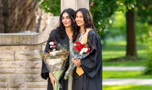 Two people in convocation robes and holding bouquets of flowers while standing in front of McMaster's Edwards Arch