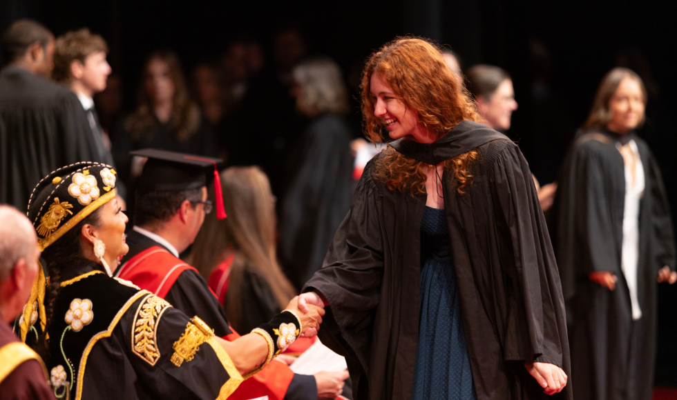 A person in a graduation gown shakes the hand of the chancellor, who is dressed in convocation regalia 