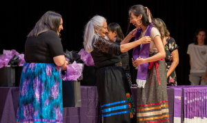 A student smiles at Kathy Knott as she places a stole around their neck at the 2024 Indigenous Graduation Celebration.
