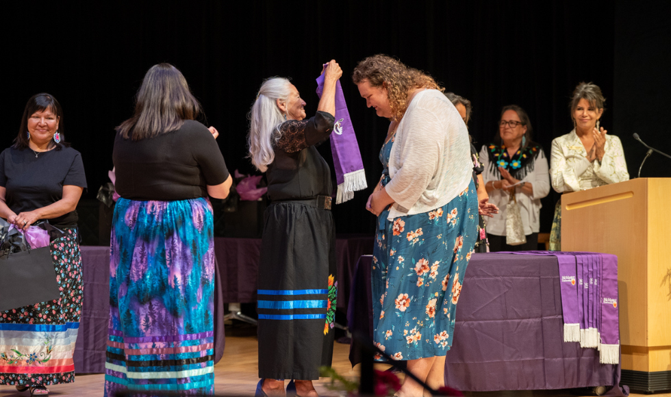 Kathy Knott reaches up to place the purple stole around a smiling student's shoulders on stage.