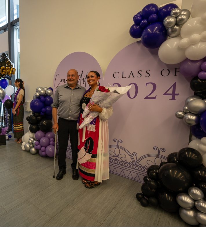 A grad and a supporter smile for a picture in front of the special backdrop.